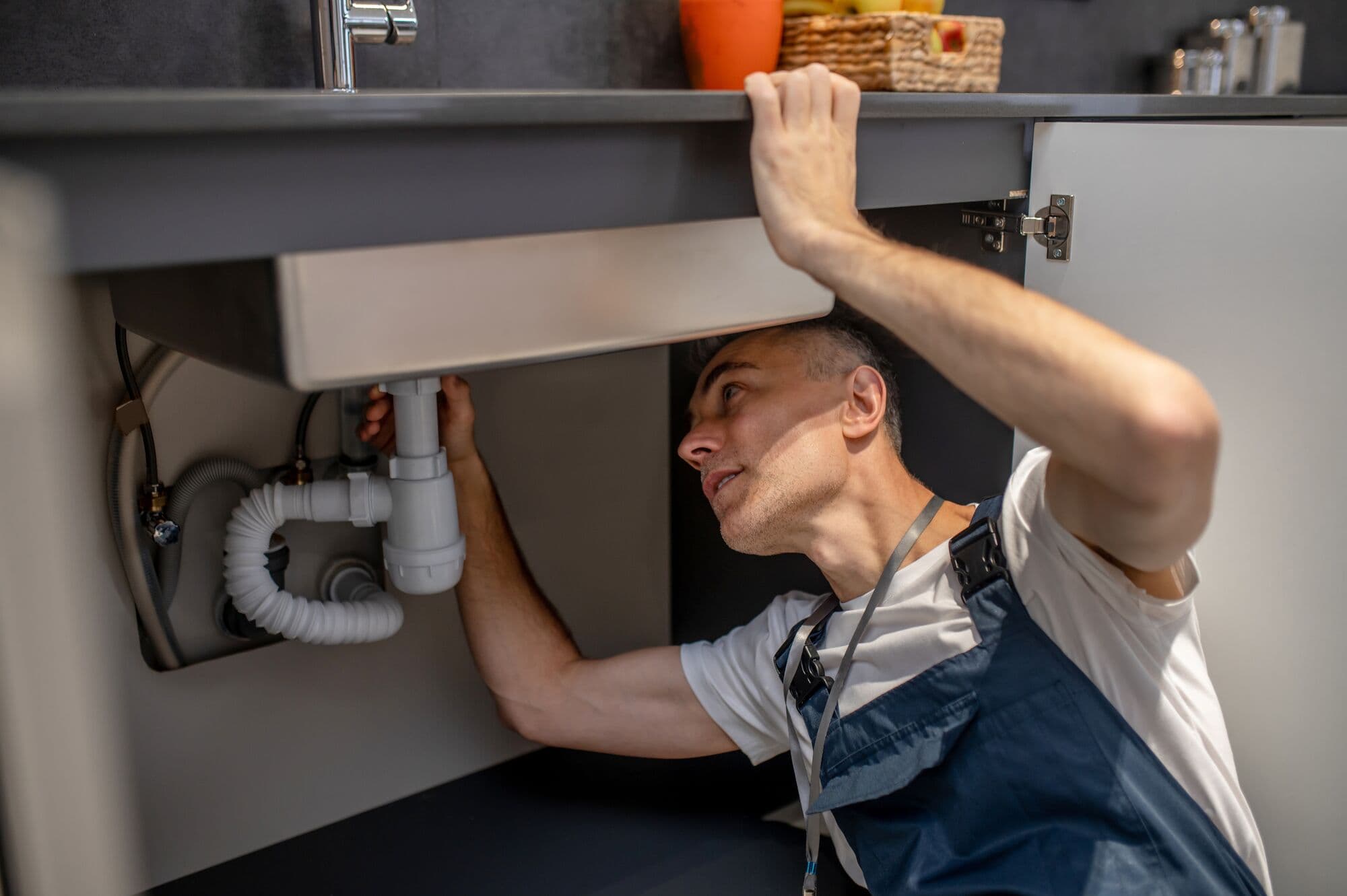 Instalatér montuje sifon pod kuchyňskou linkou